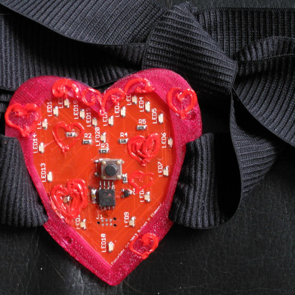 PCB of heart with a button and LEDs on a black cloth background.
